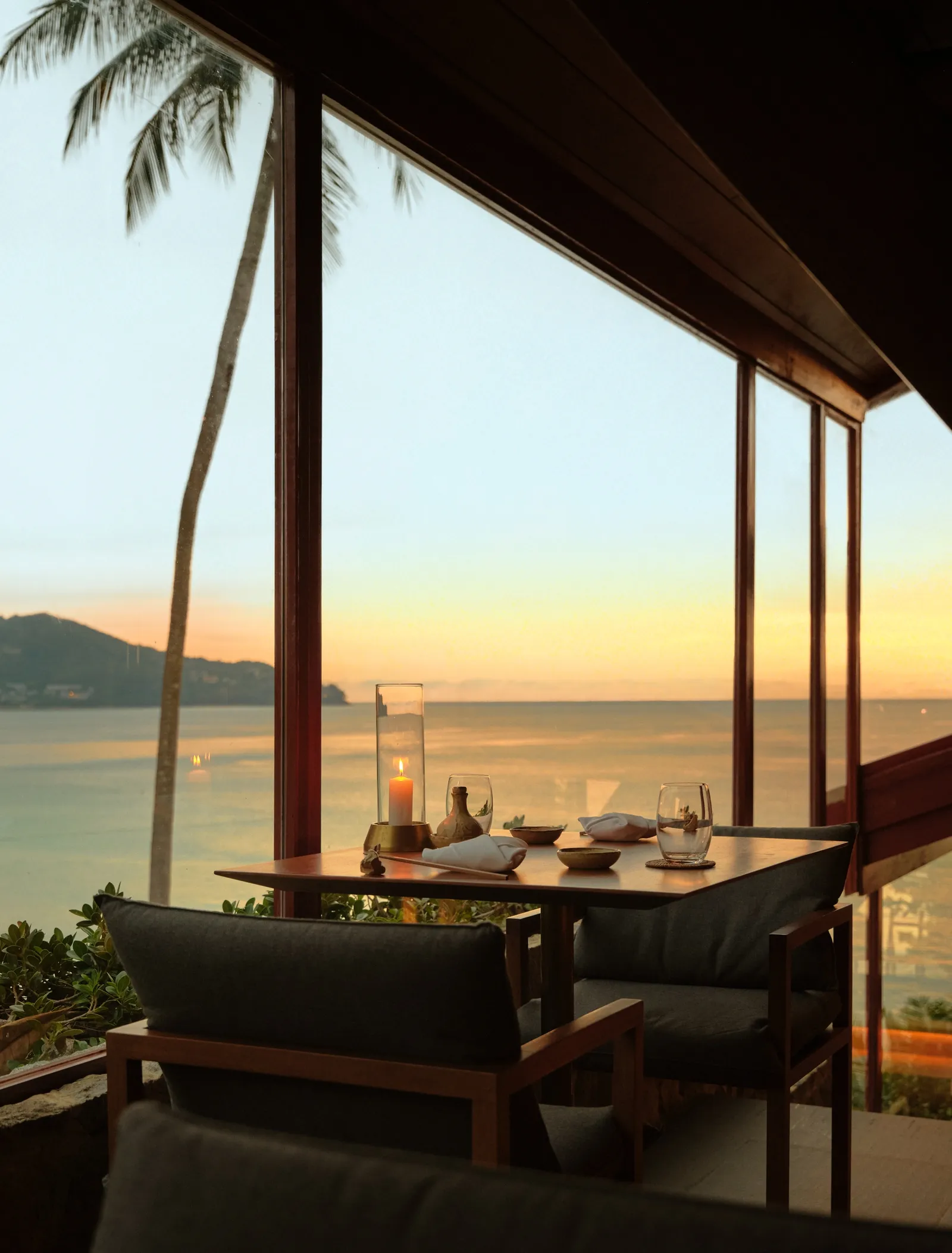 Akari at sunset: a table on the wooden terrace above the bay, palms and the sea beyond