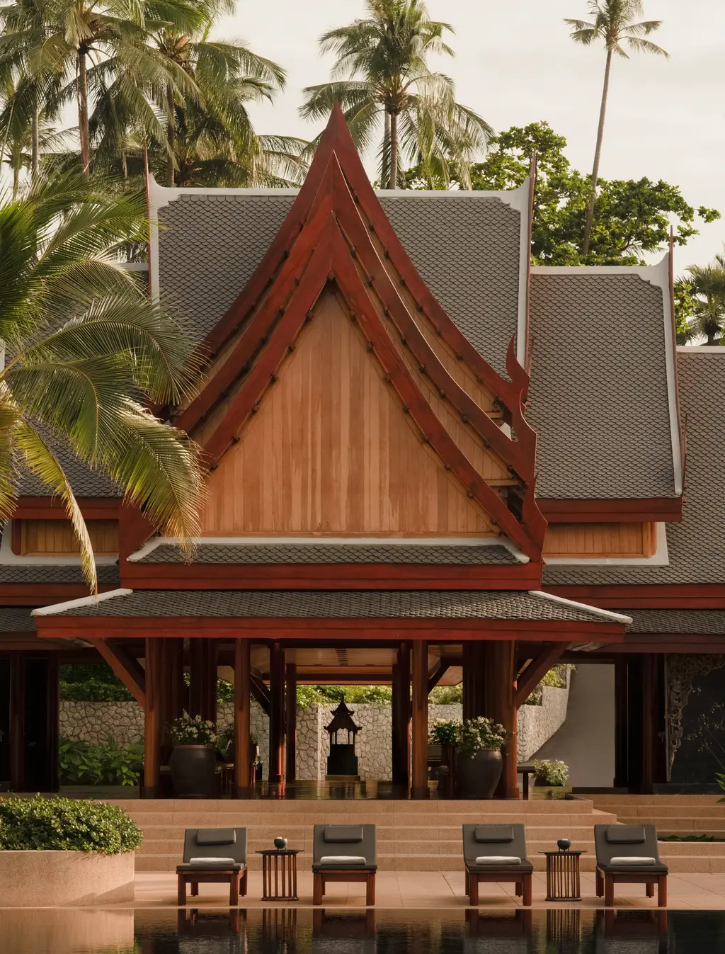 The arrival pavilion: a tiered teak roof over an open hall, loungers along the pool in front