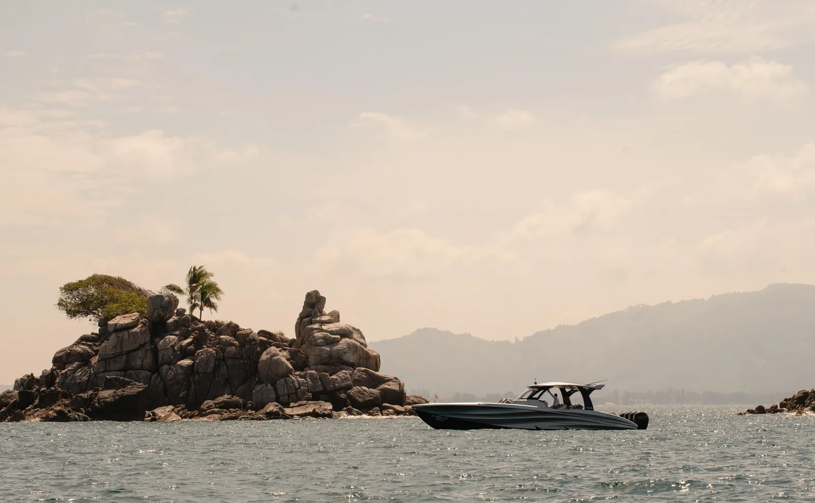 A speedboat off a rocky islet in the Andaman Sea, hills on the horizon