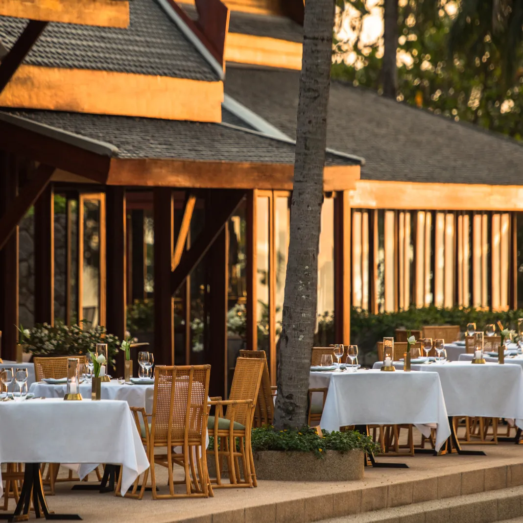 Buabok’s terrace at dusk: tables laid with white cloths under the teak eaves