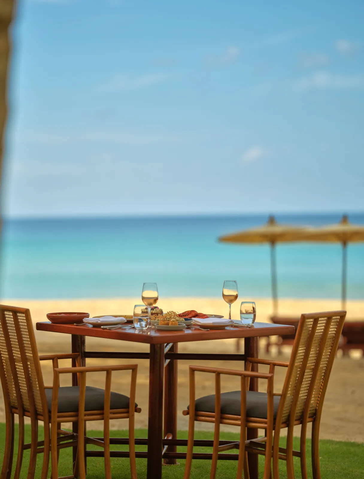 A table for 2 at Nura on the sand, under a parasol, the sea behind