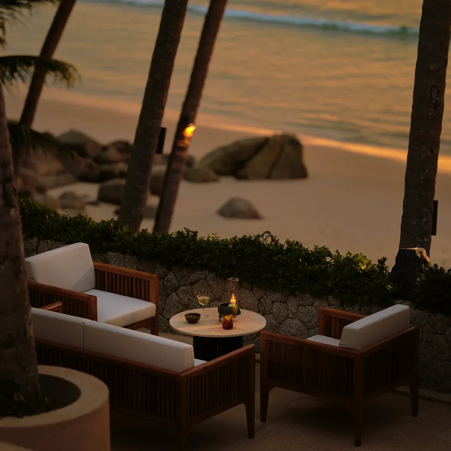 The Sunset Terrace at dusk: armchairs and a low table above the rocks and the beach