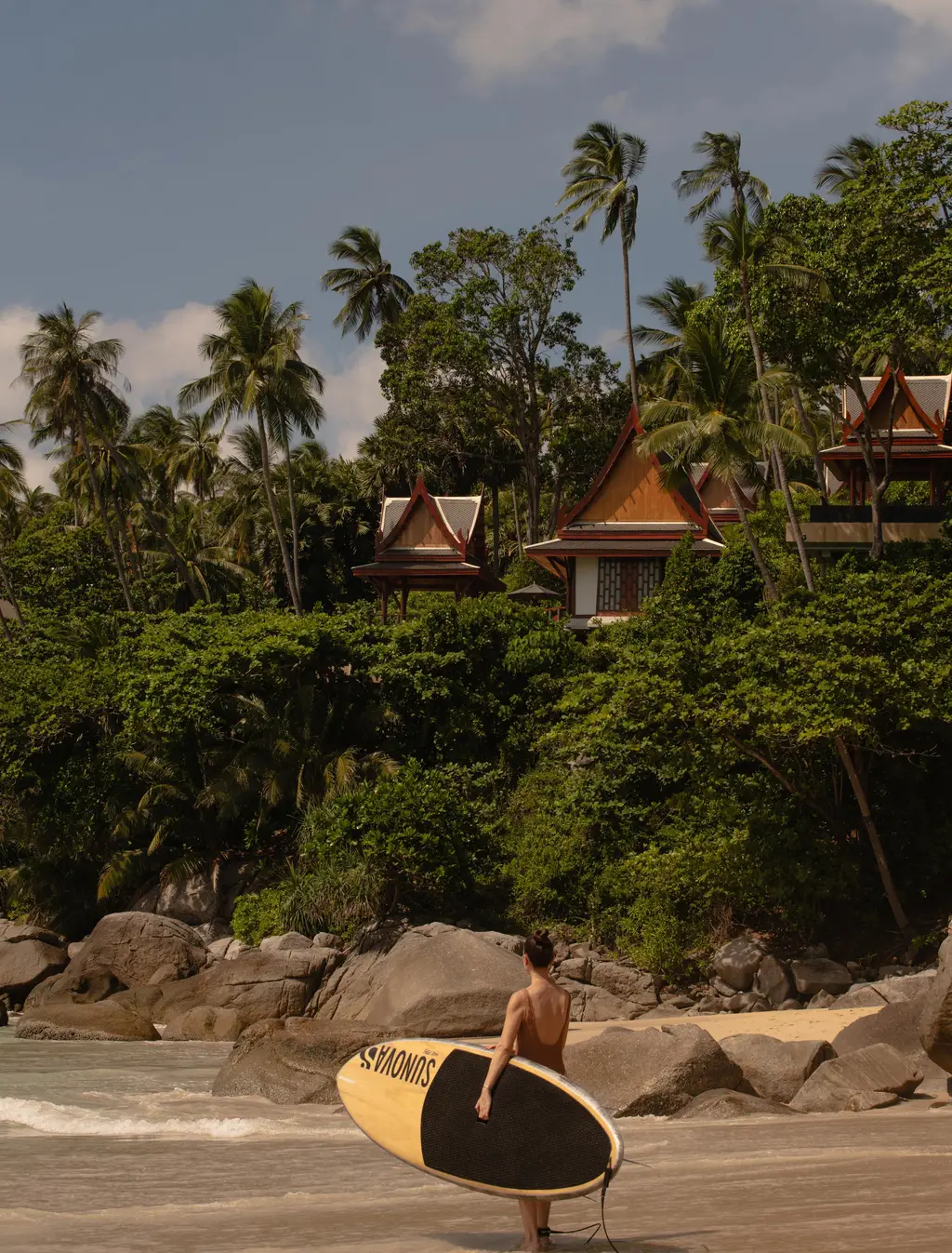A paddleboarder carrying a board on Pansea Beach, villas on the hill behind