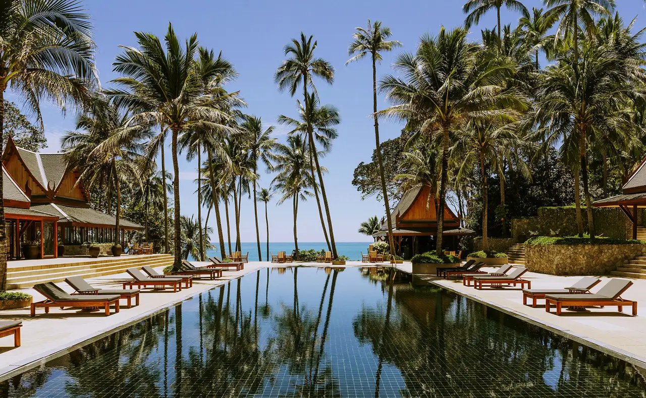 The dark-tiled main pool between coconut palms, Thai pavilions on each side and the sea at the end
