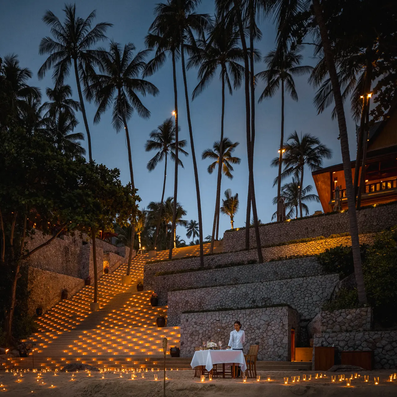 The stone steps to the beach at dusk, lit by hundreds of candles, a table laid at their foot