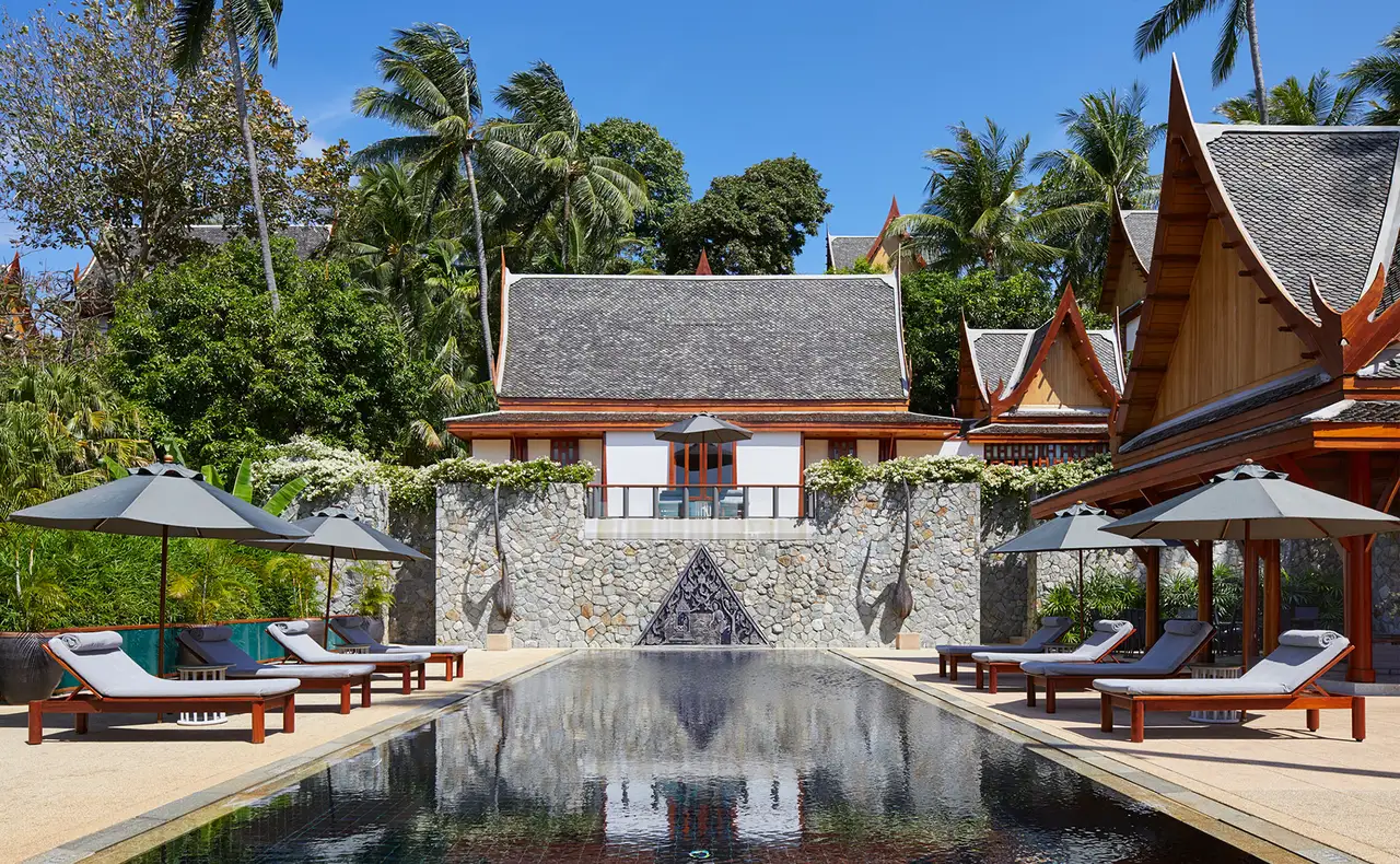 A villa pool in front of a stone-walled pavilion
