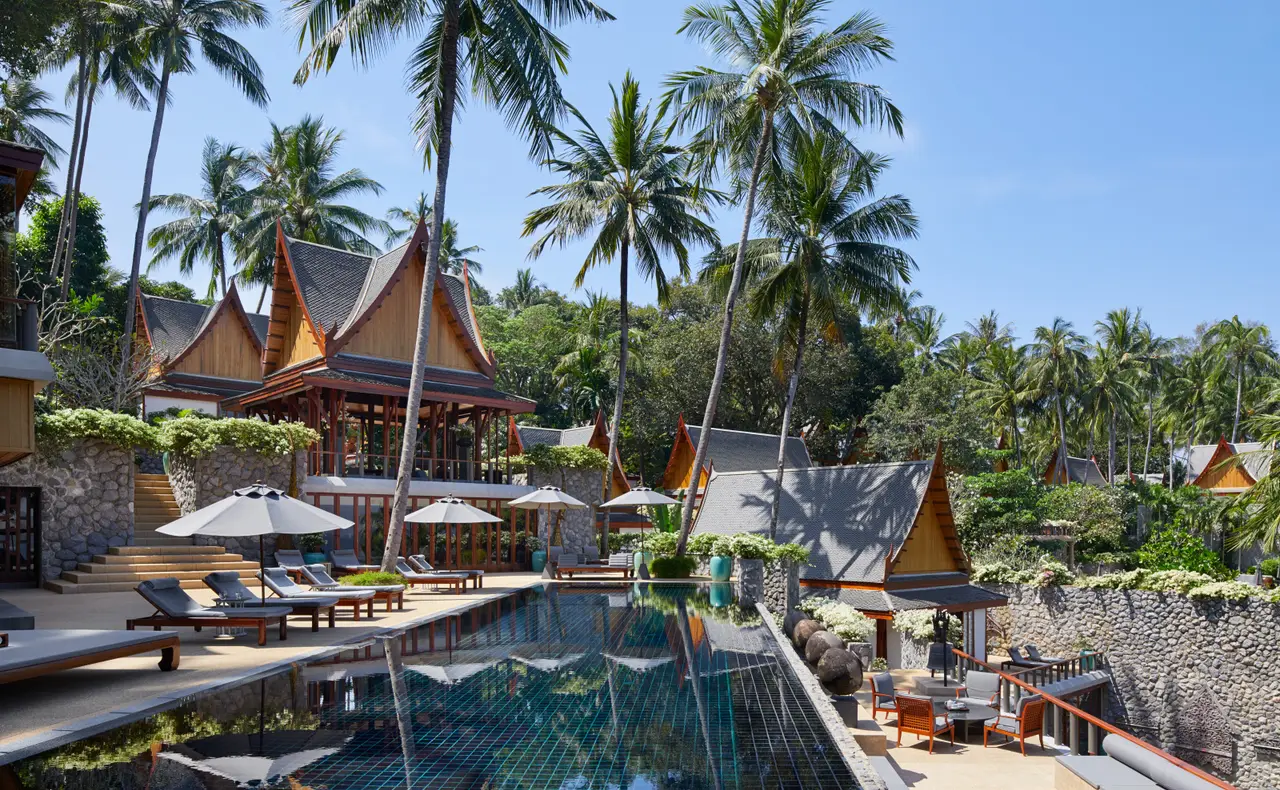 A terrace of loungers along a villa pool among palms
