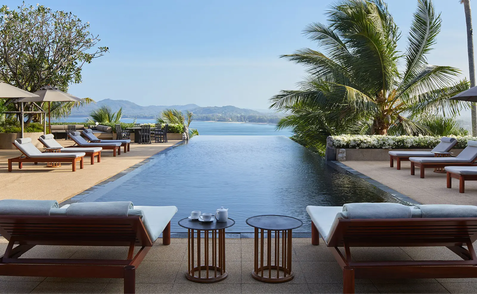 An infinity pool running towards the sea, 2 loungers in front