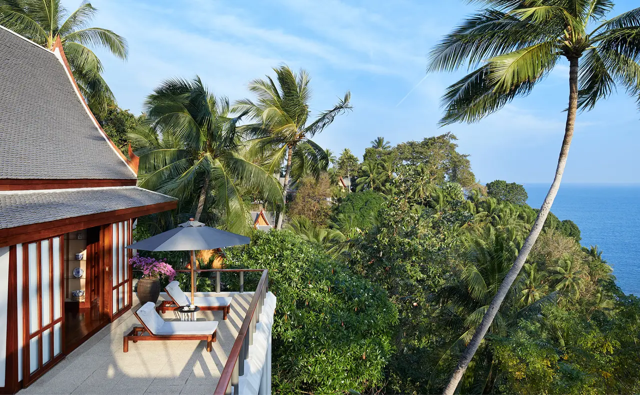 A villa pavilion with loungers on a terrace above the forested coast and the sea