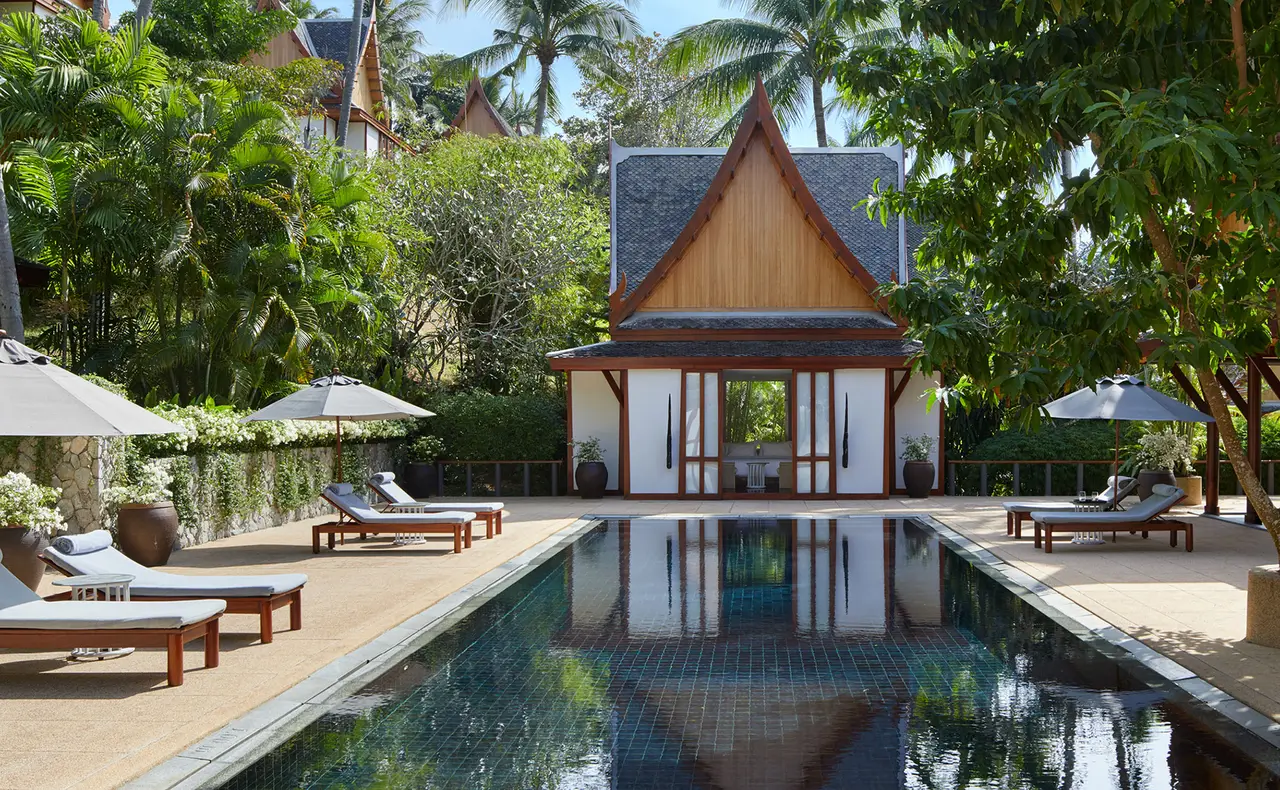 A villa’s pool reflecting a white Thai pavilion, loungers on both sides