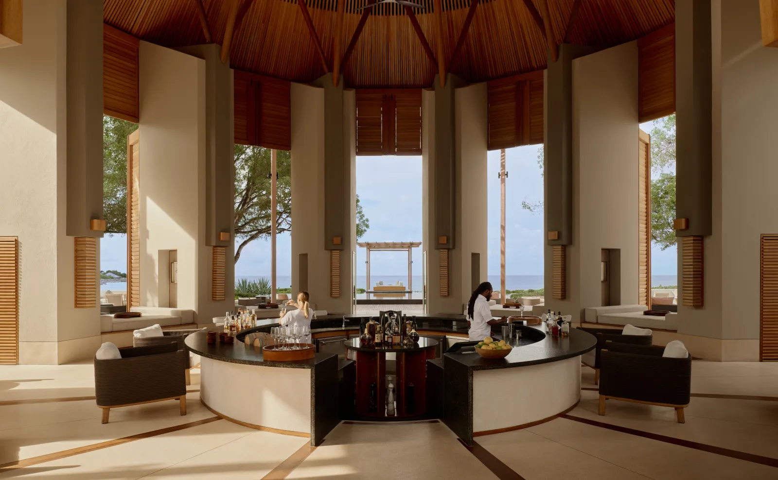 The bar’s round interior: the counter in the middle, 2 bartenders at work and tall openings towards the sea.