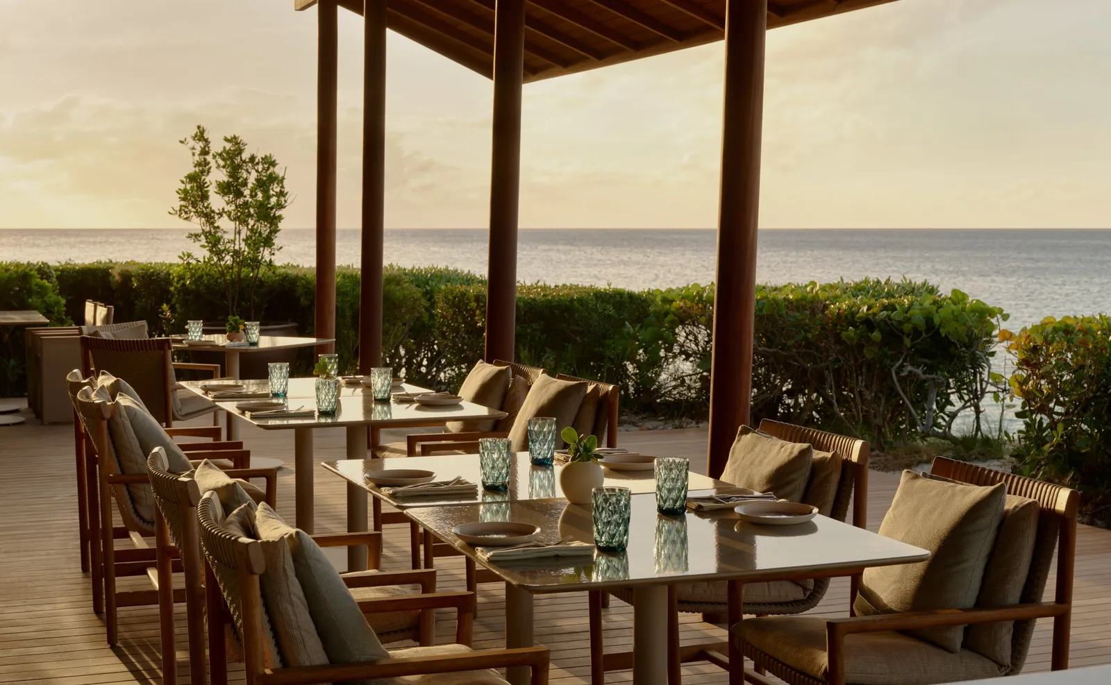 A laid table on the Beach Club’s covered terrace, with hedges and the sea at sunset.