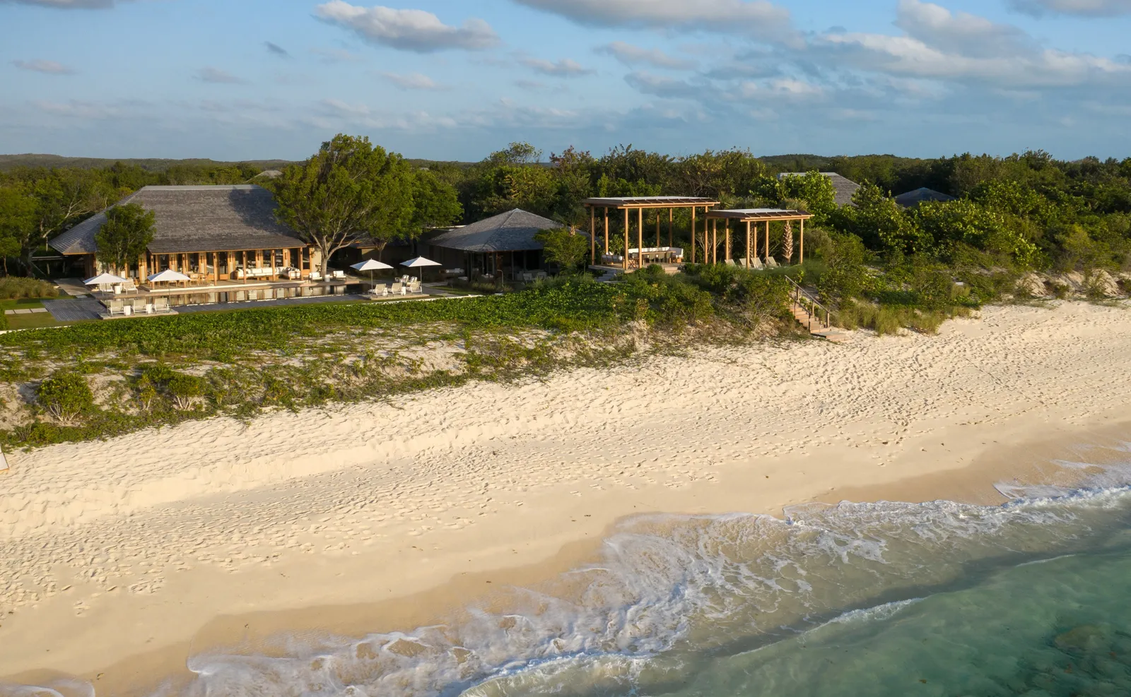 The beach seen from the sea: pale sand, the dune with its shrubs and a villa’s pavilions on top.