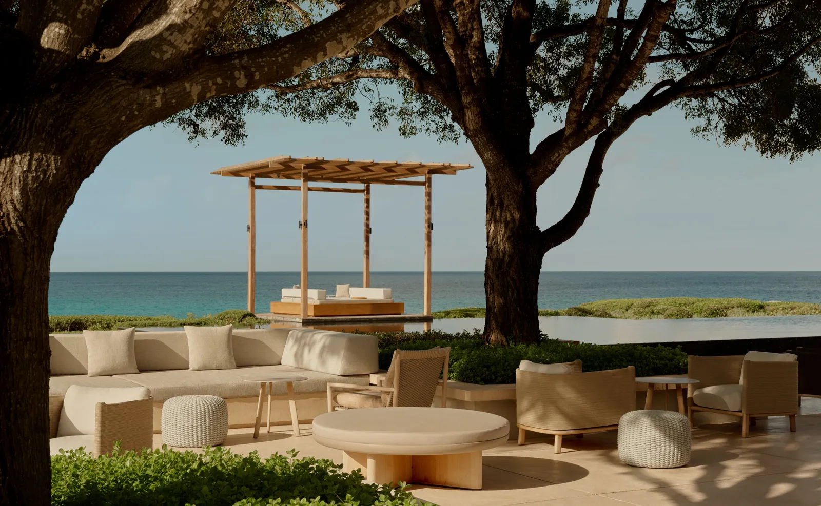 The bar terrace under 2 large trees: pale sofas, the infinity pool and a timber sala before the ocean.