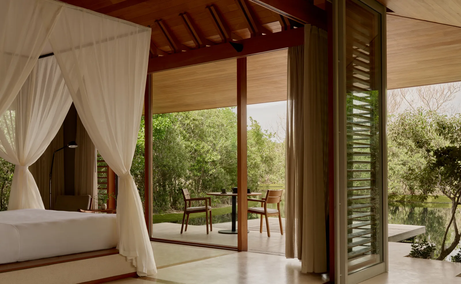 Inside a pond pavilion: the canopied bed, sliding doors open and the terrace with 2 chairs.