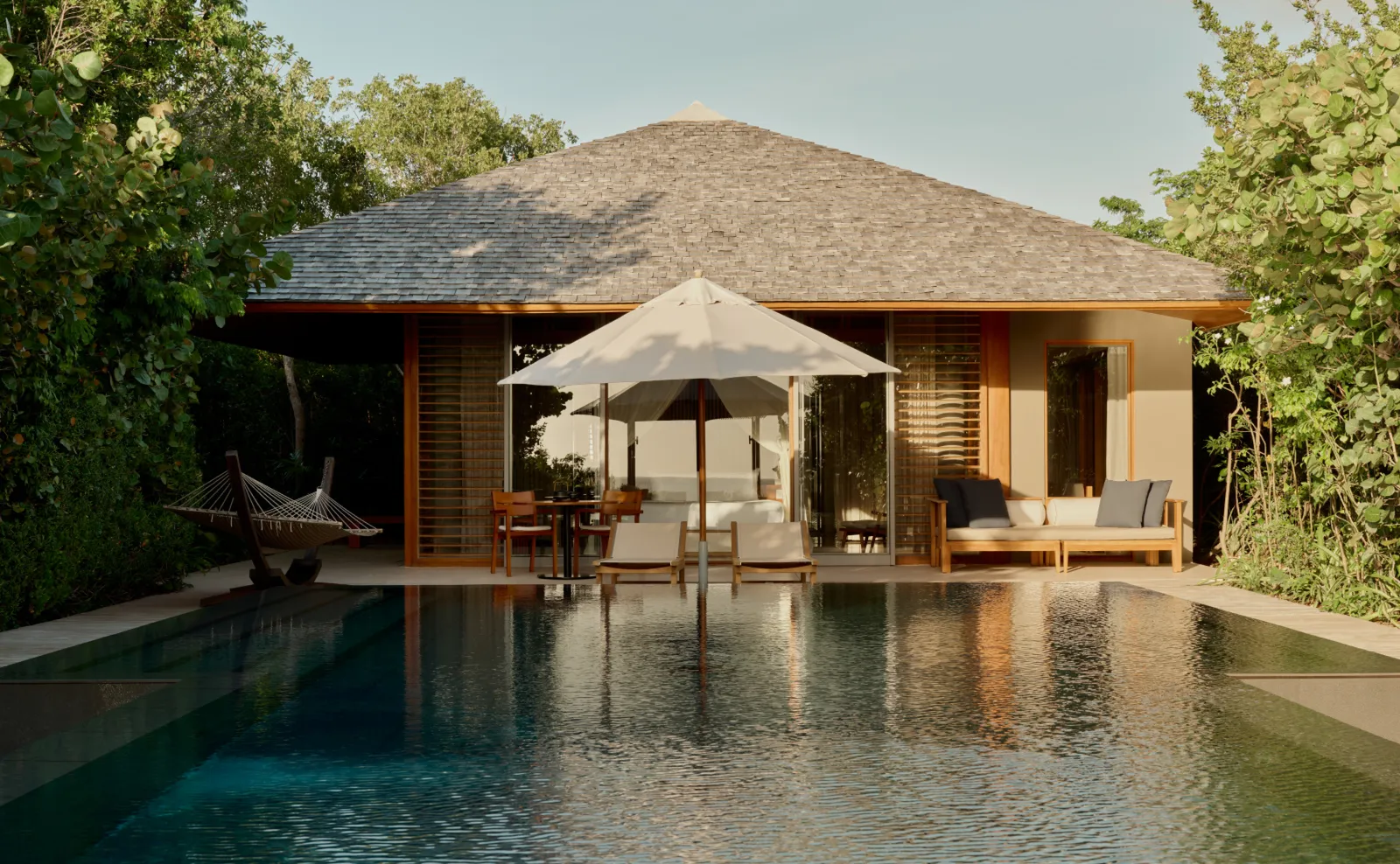 The Amanyara Pavilion from its pool: a parasol, a hammock, a sofa on the deck and trees around.