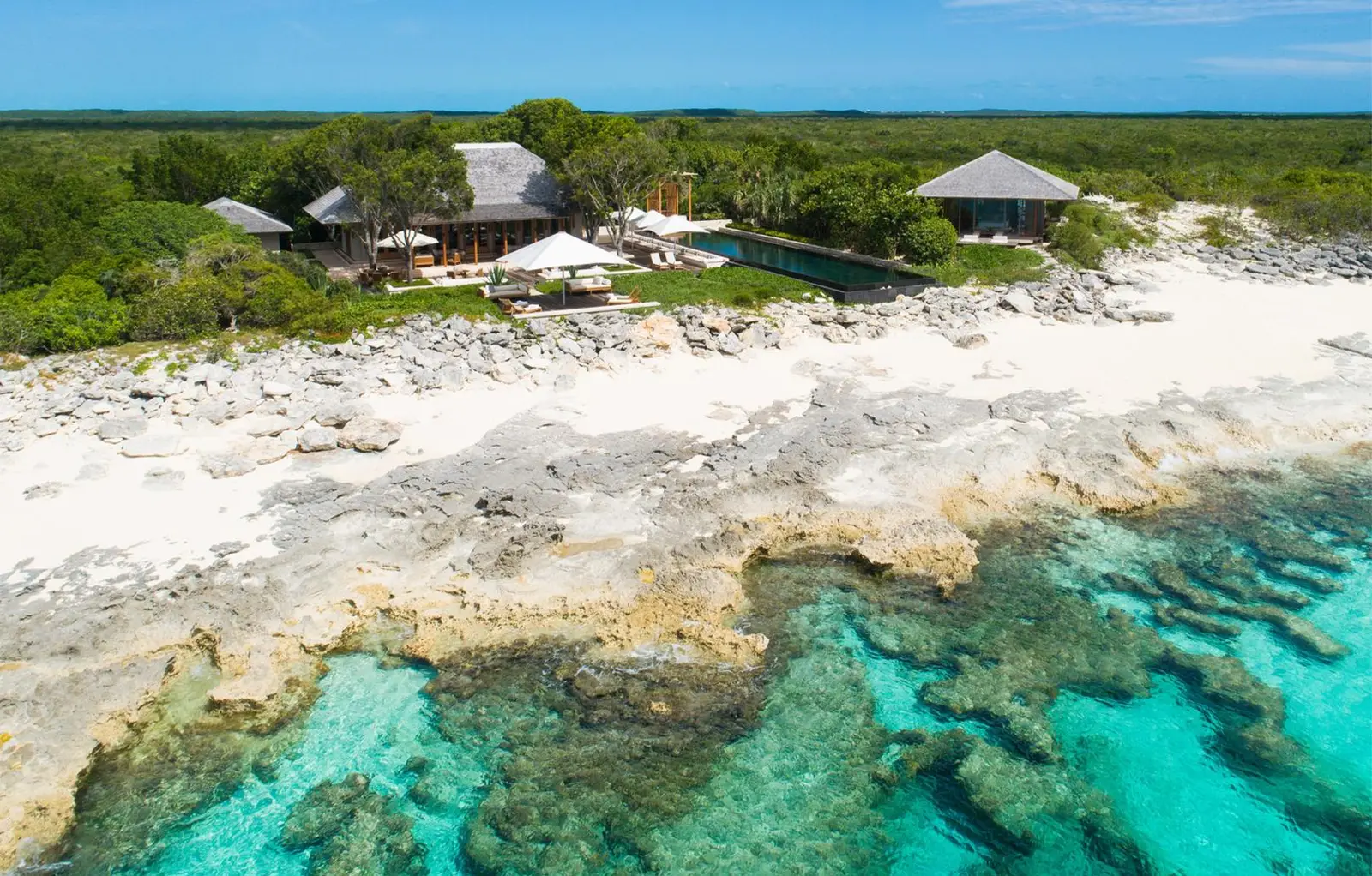 The Artists Villa from above: pavilions and pool above the pale shore rock, the reef under turquoise water.