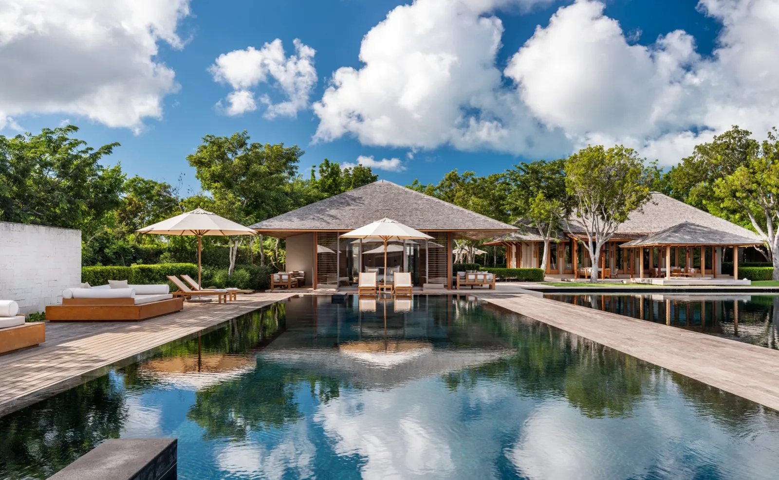 The 5-bedroom Serenity Villa: clouds reflected in the large dark pool, pavilions and parasols at the far end.