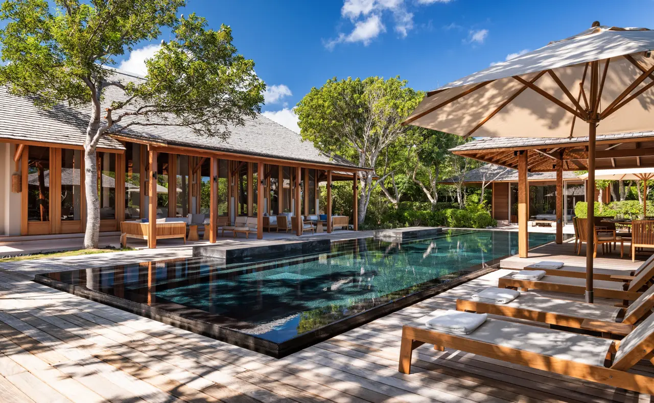 A villa’s dark stone pool, loungers under parasols and the glazed central pavilion.