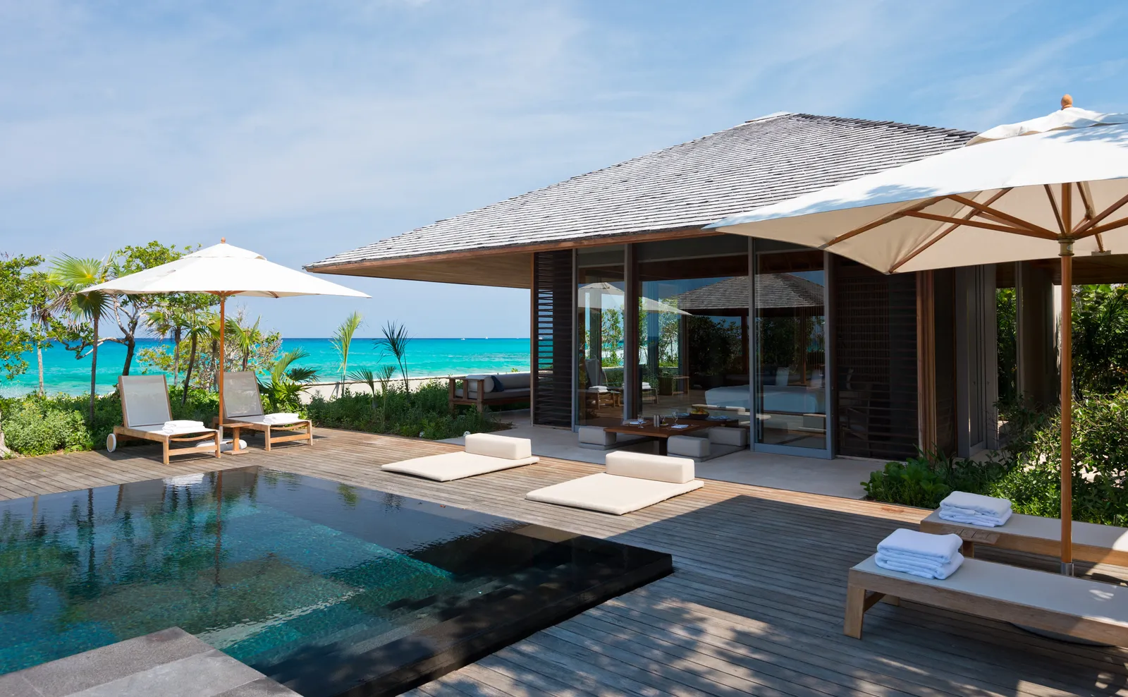 An Ocean Villa’s deck: the dark pool, loungers under parasols and the turquoise sea beyond the shrubs.