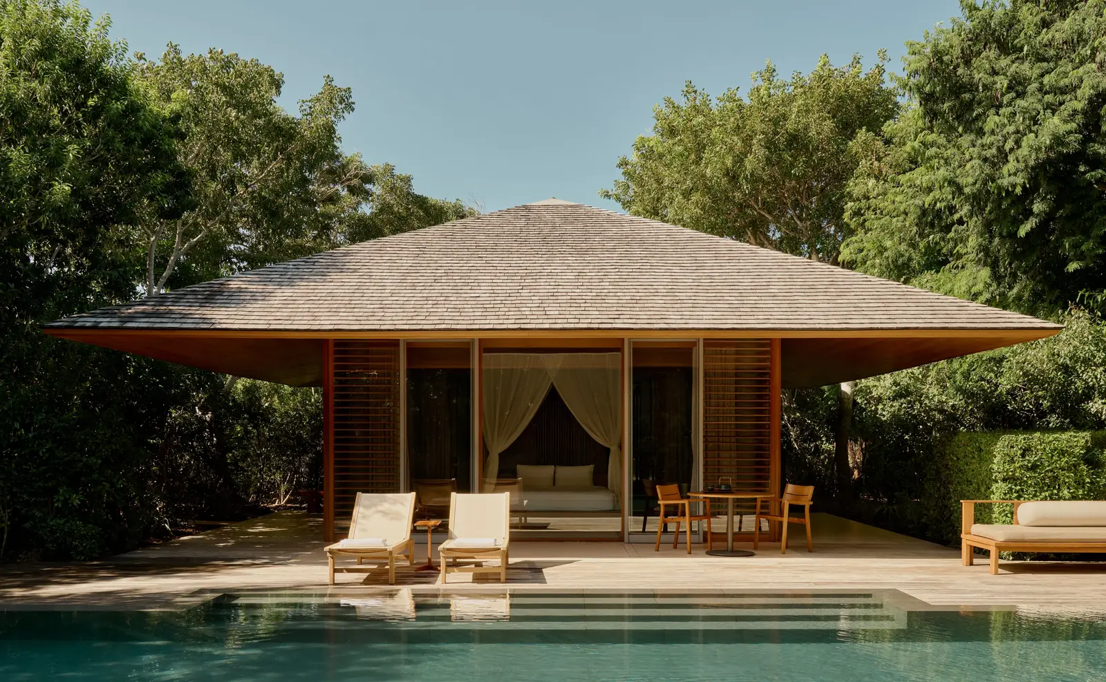 An Ocean Pool Pavilion: the shingle roof, loungers and the private pool enclosed by vegetation.