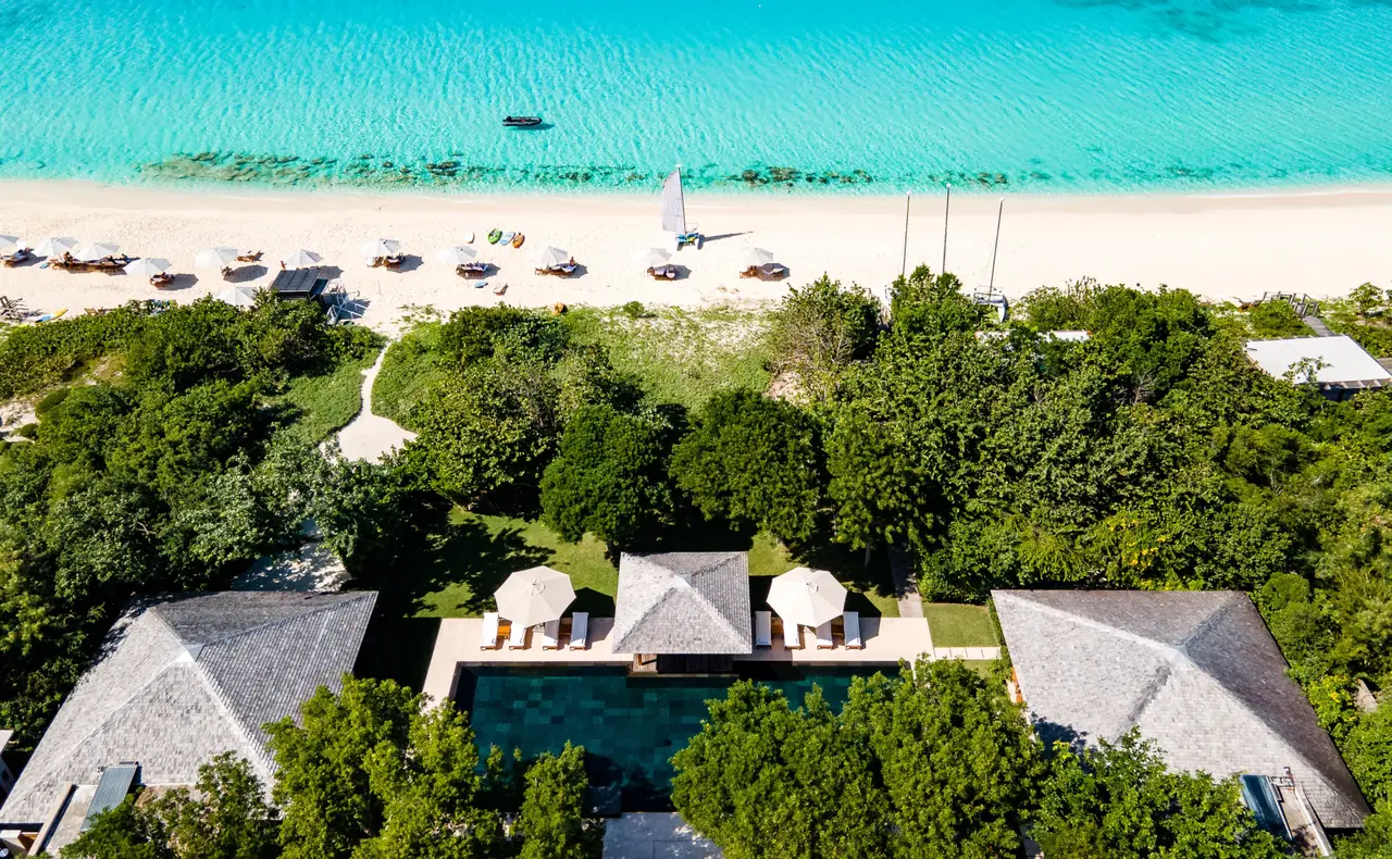 The Amanyara Villa from above: roofs and pool among trees, and just beyond them the beach with its parasols and the shallows.