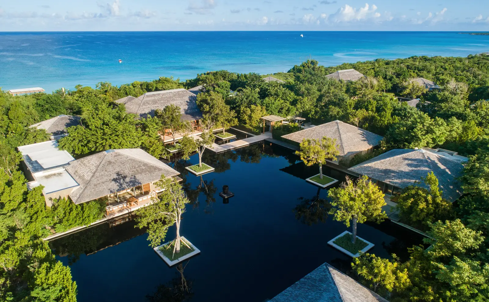 The 6-bedroom villa from above: pavilions round a dark pond with small tree islands, the sea on the horizon.