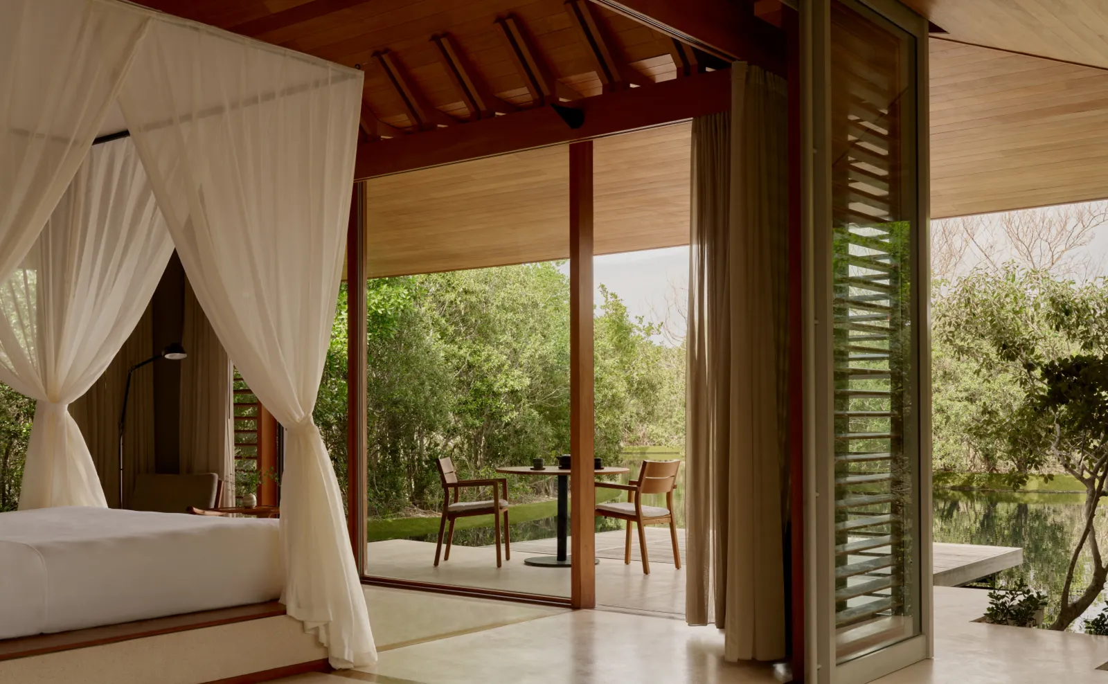 A Tranquility Pavilion: the bed under its canvas canopy and the terrace with a table and 2 chairs, open to the greenery.