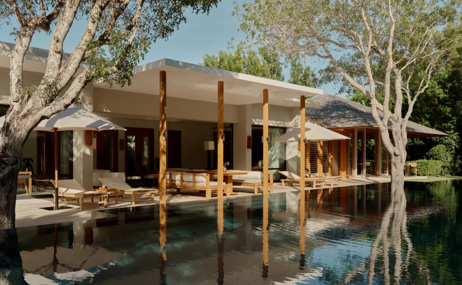 The Two-Bedroom Pool Pavilion Suite: low pavilions and loungers mirrored in the dark pool, among trees.