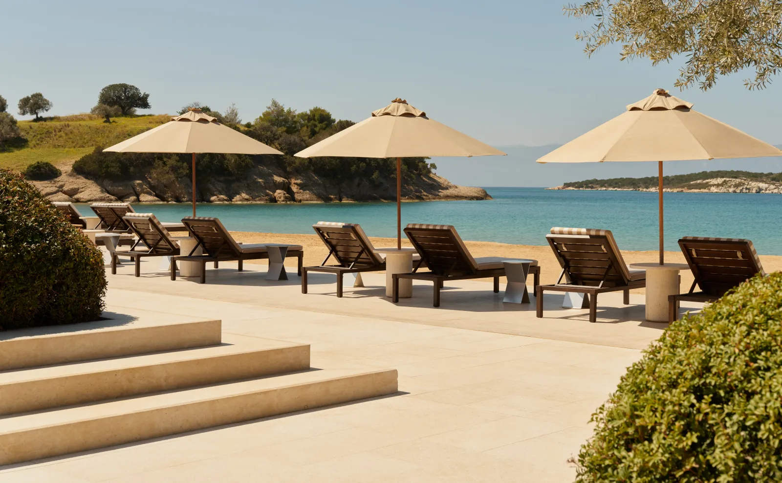 The Beach Club terrace: wooden loungers under sand-coloured parasols, facing the beach and the bay.