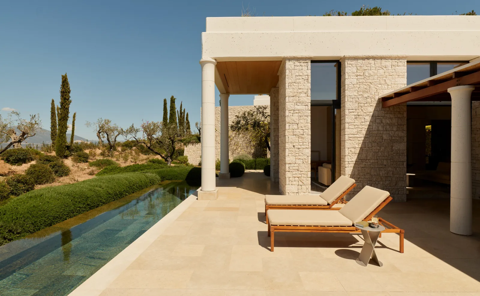 A Deluxe Pool Pavilion: the 12-metre pool beside the terrace, 2 loungers and the pale stone pavilion.