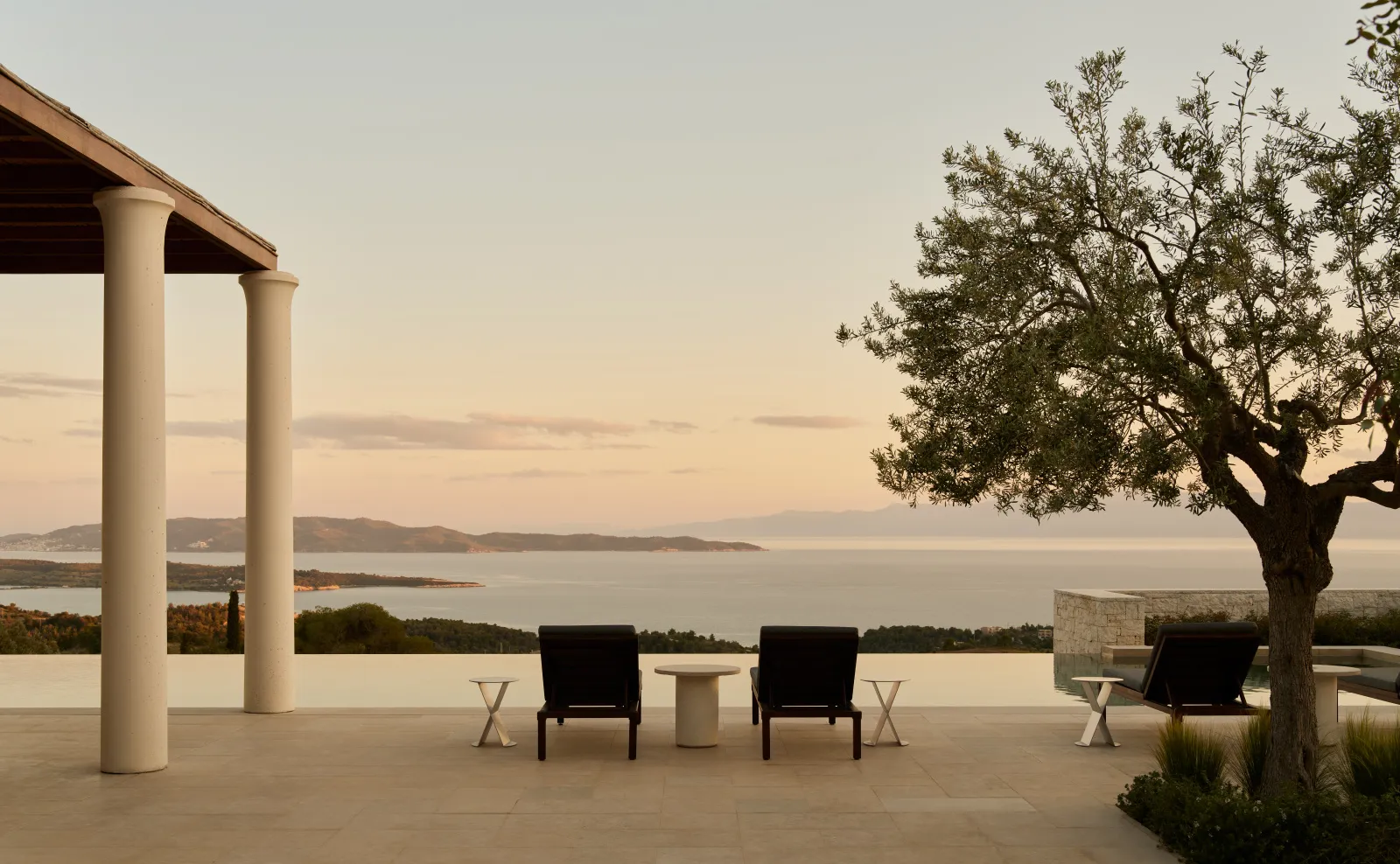 A 4-bedroom villa’s terrace at sunset: 2 black chairs, an olive tree and the sea with its islands.