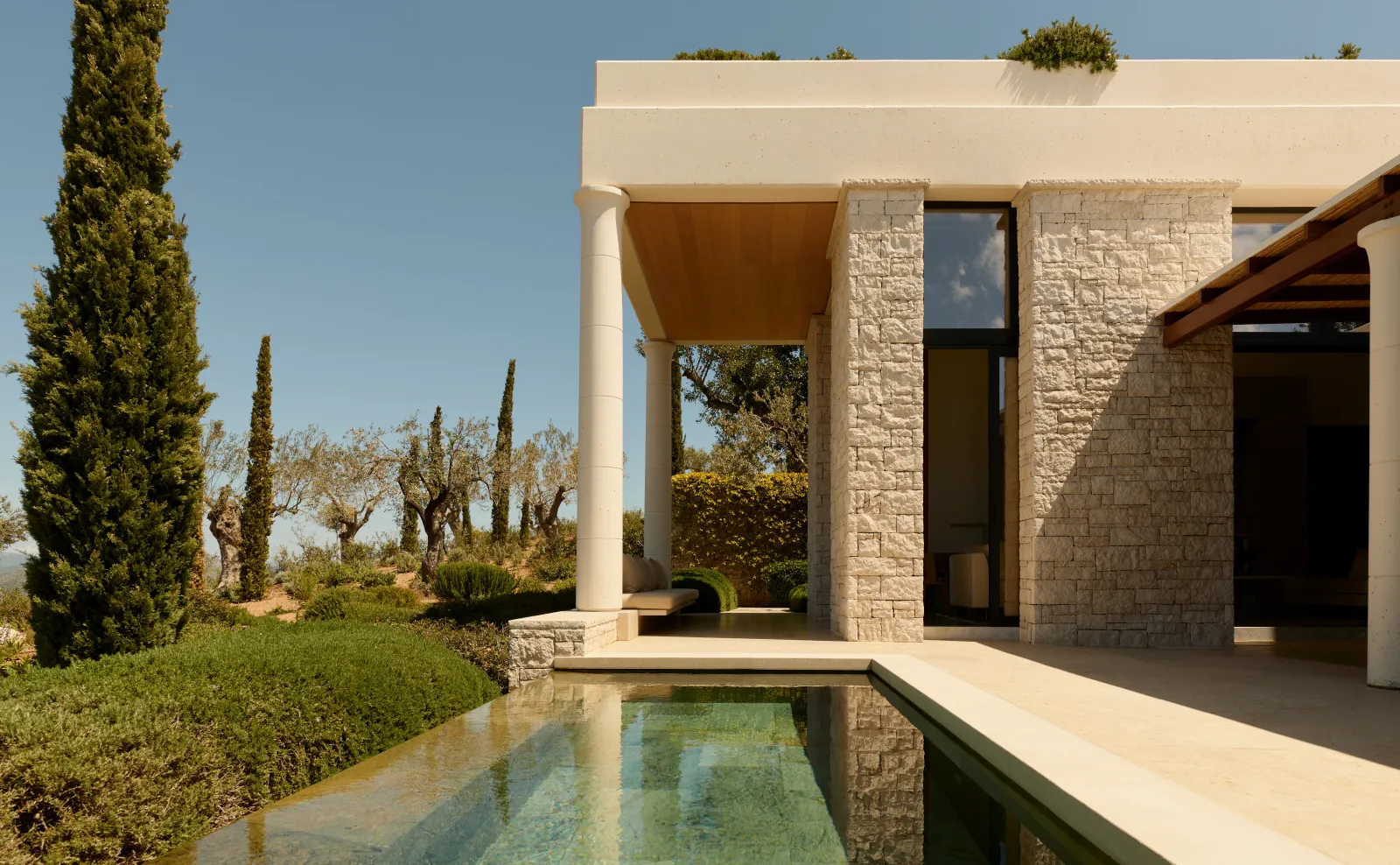 A Pool Pavilion: the pool running along the stone terrace, the pergola on columns, a cypress and the countryside.