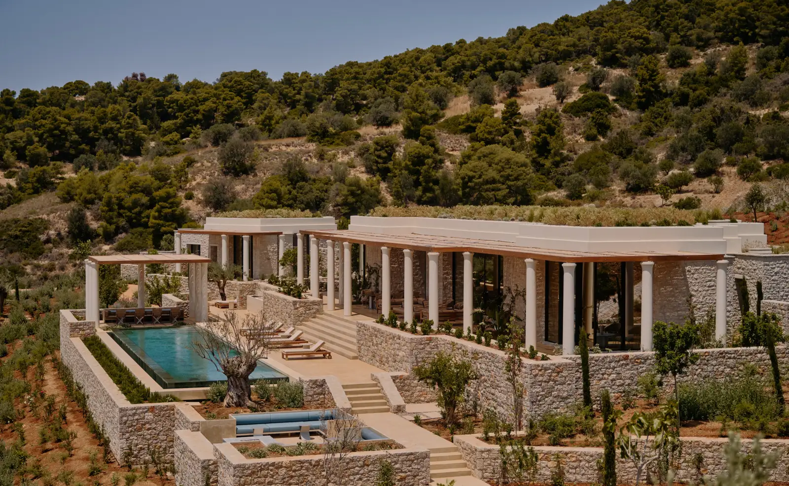 The 3-bedroom villa on the hillside: colonnaded porticoes, the pool and stone terraces among pines.