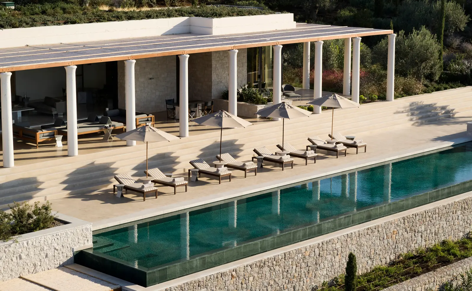 A 2-bedroom villa: the white colonnade, parasols and loungers above the stone-edged infinity pool.