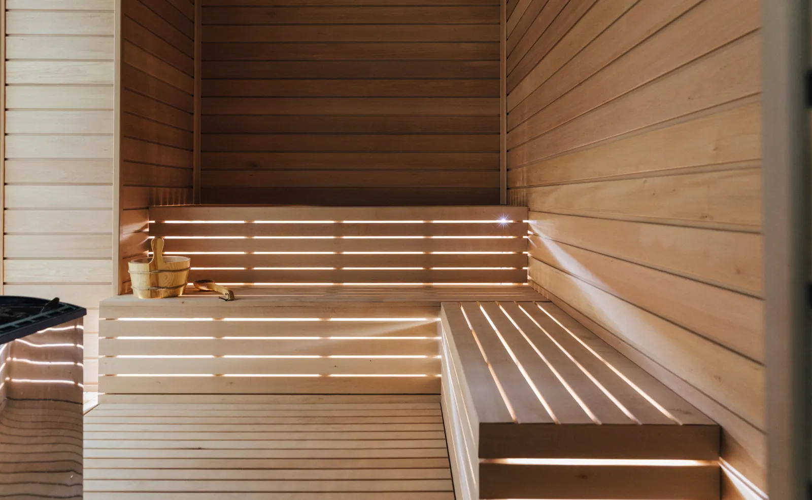 The spa’s sauna: pale timber benches on 2 levels, lit from beneath, and the bucket with its ladle.