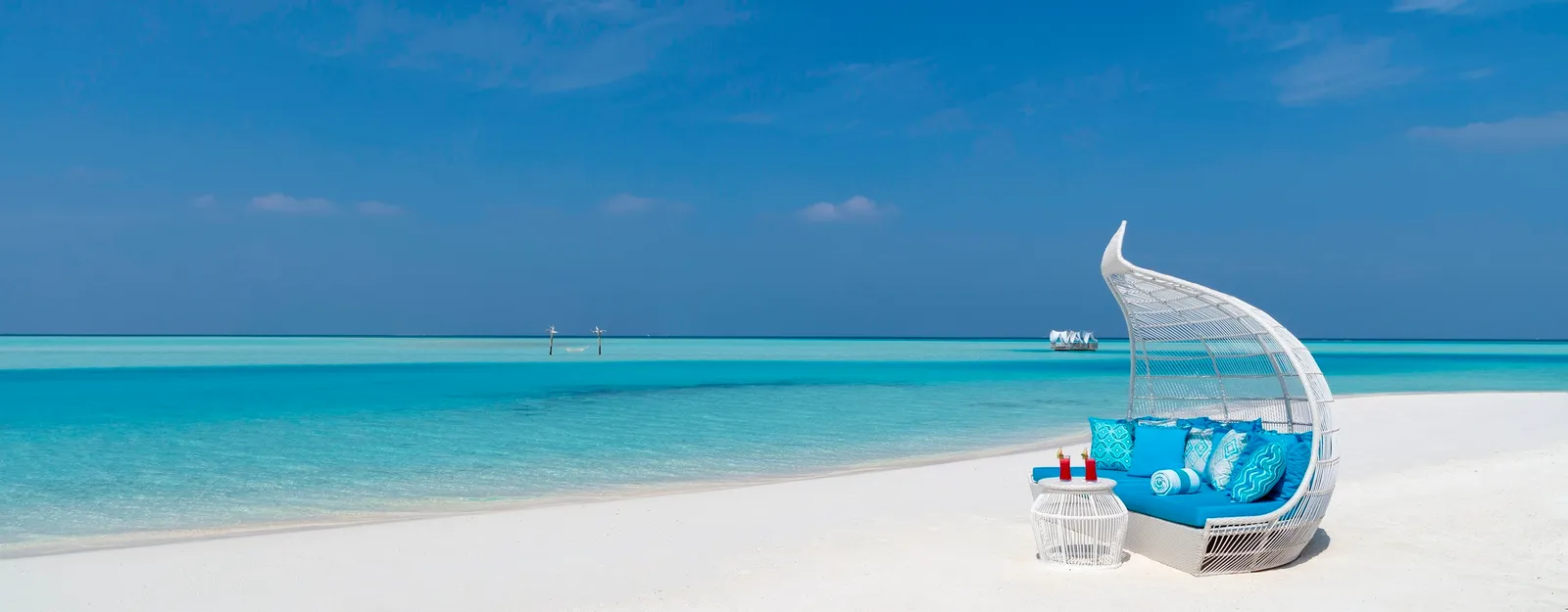 Un divanetto a conchiglia con i cuscini blu sulla spiaggia bianca, davanti alla laguna.
