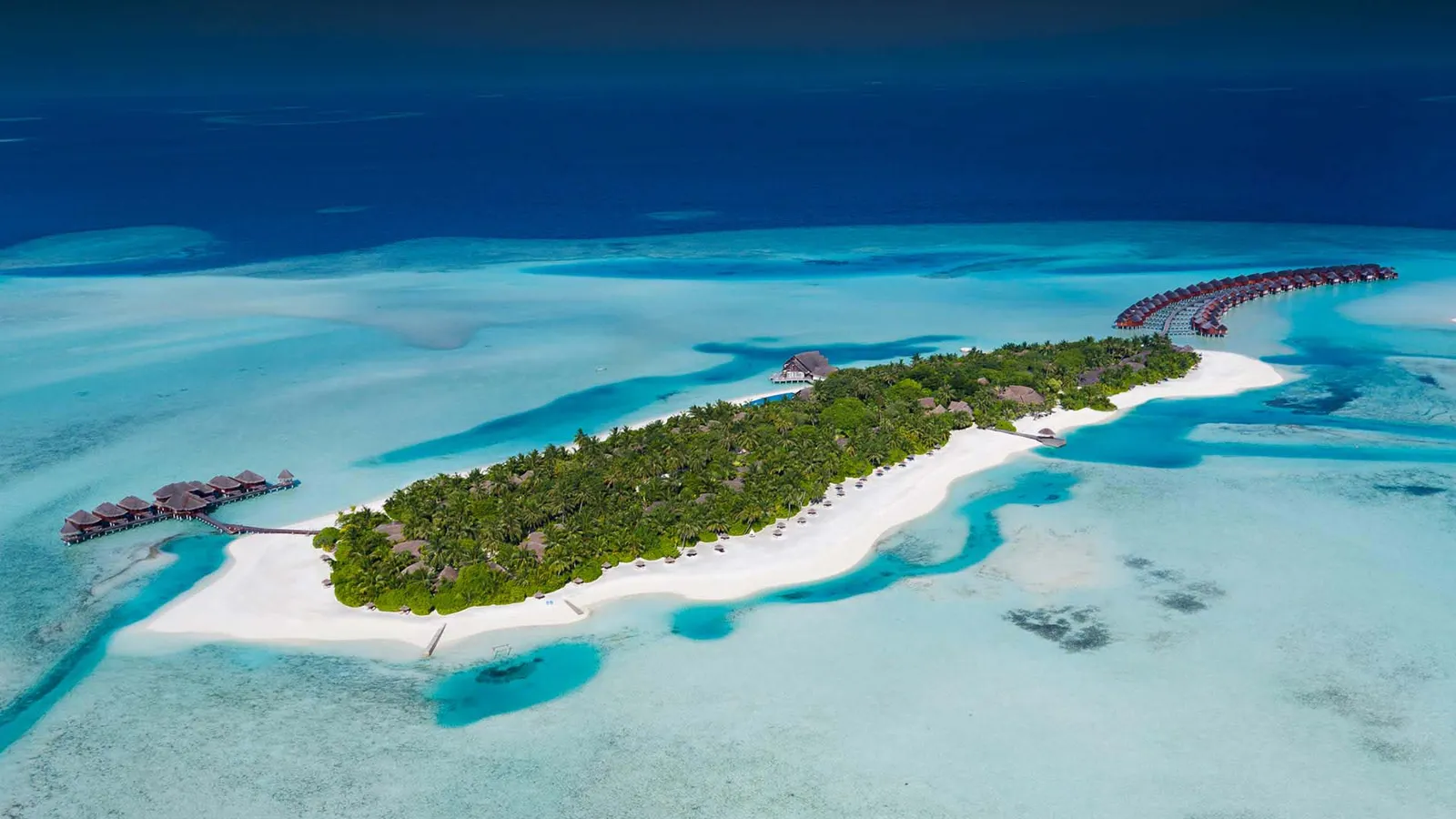 Dhigufinolhu dall’alto: l’isola lunga e verde, la spiaggia bianca su un lato e le ville sull’acqua che escono nella laguna.
