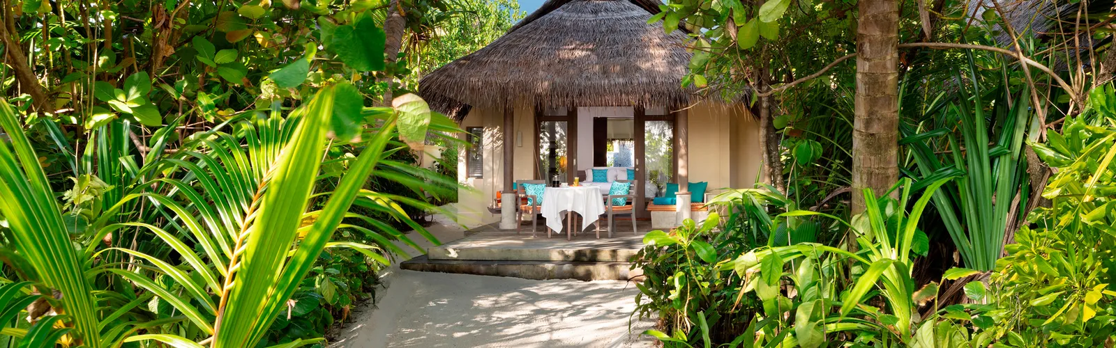 Il vialetto fra le piante che porta alla Sunrise Beach Villa, con il tetto di paglia e il tavolo sulla terrazza.