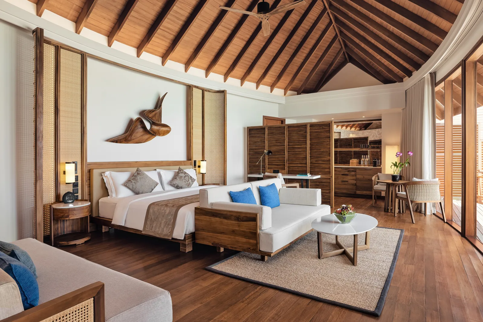 La camera di una villa sull’acqua rinnovata nel 2024: il letto, il divano e il soffitto di legno a capanna.