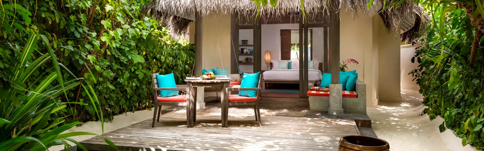 La Sunset Beach Villa dal cortile: il letto oltre le porte aperte, la terrazza con il tavolo e il verde intorno.