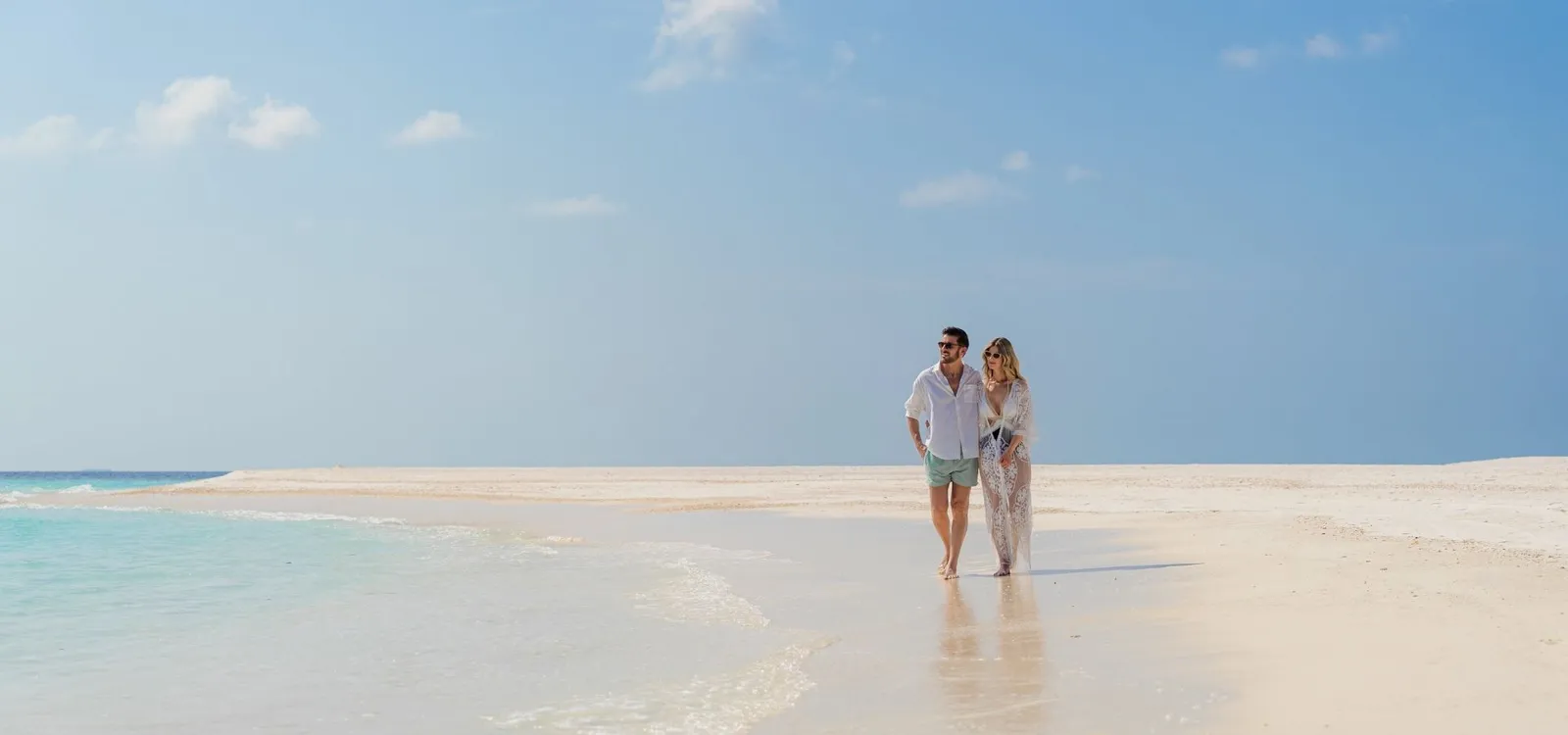 A couple walking along the spit of sand, shallow water all around