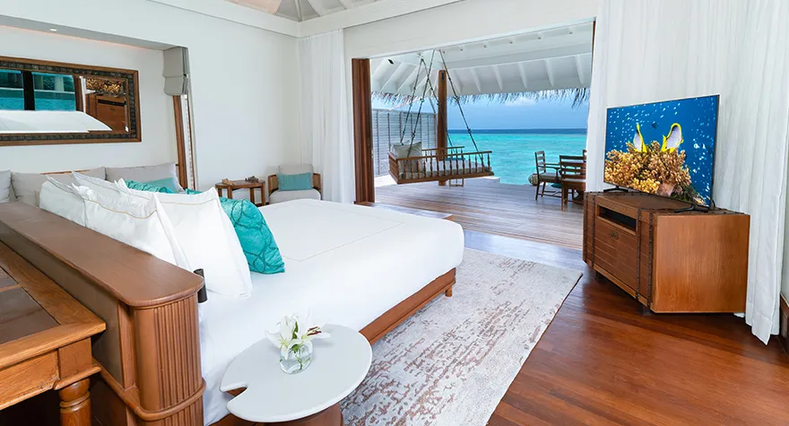 An Over Water Pool Villa’s bedroom, the bed and the lagoon beyond the glass