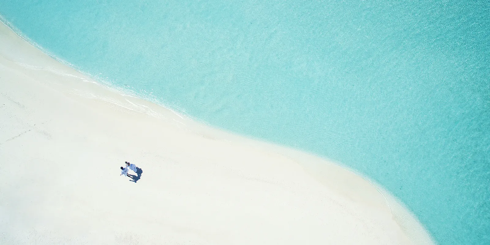 A white sandbank in the lagoon from above, 2 people and an umbrella