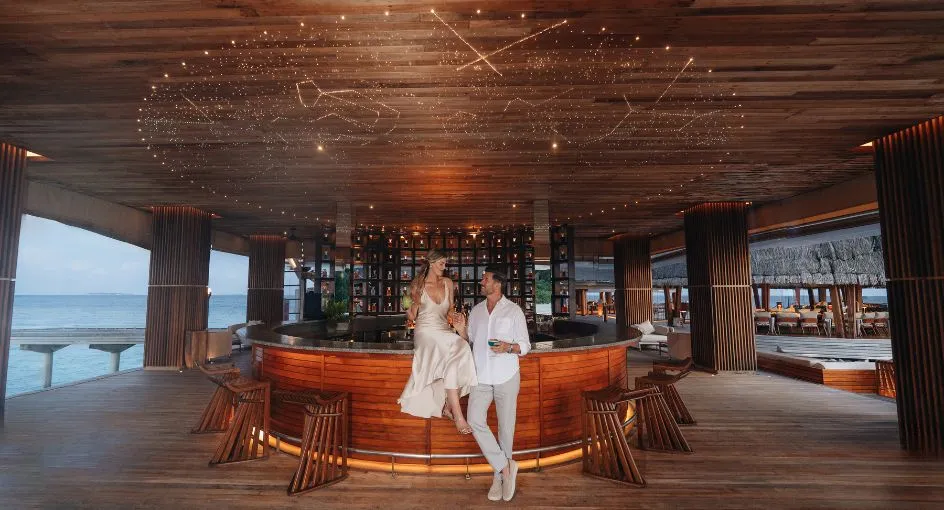 A couple at SKY’s bar, bottles behind them and the sea beyond the windows