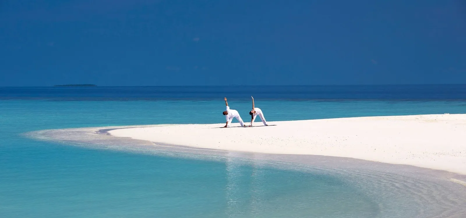2 people doing yoga on the sand spit, blue sea all around