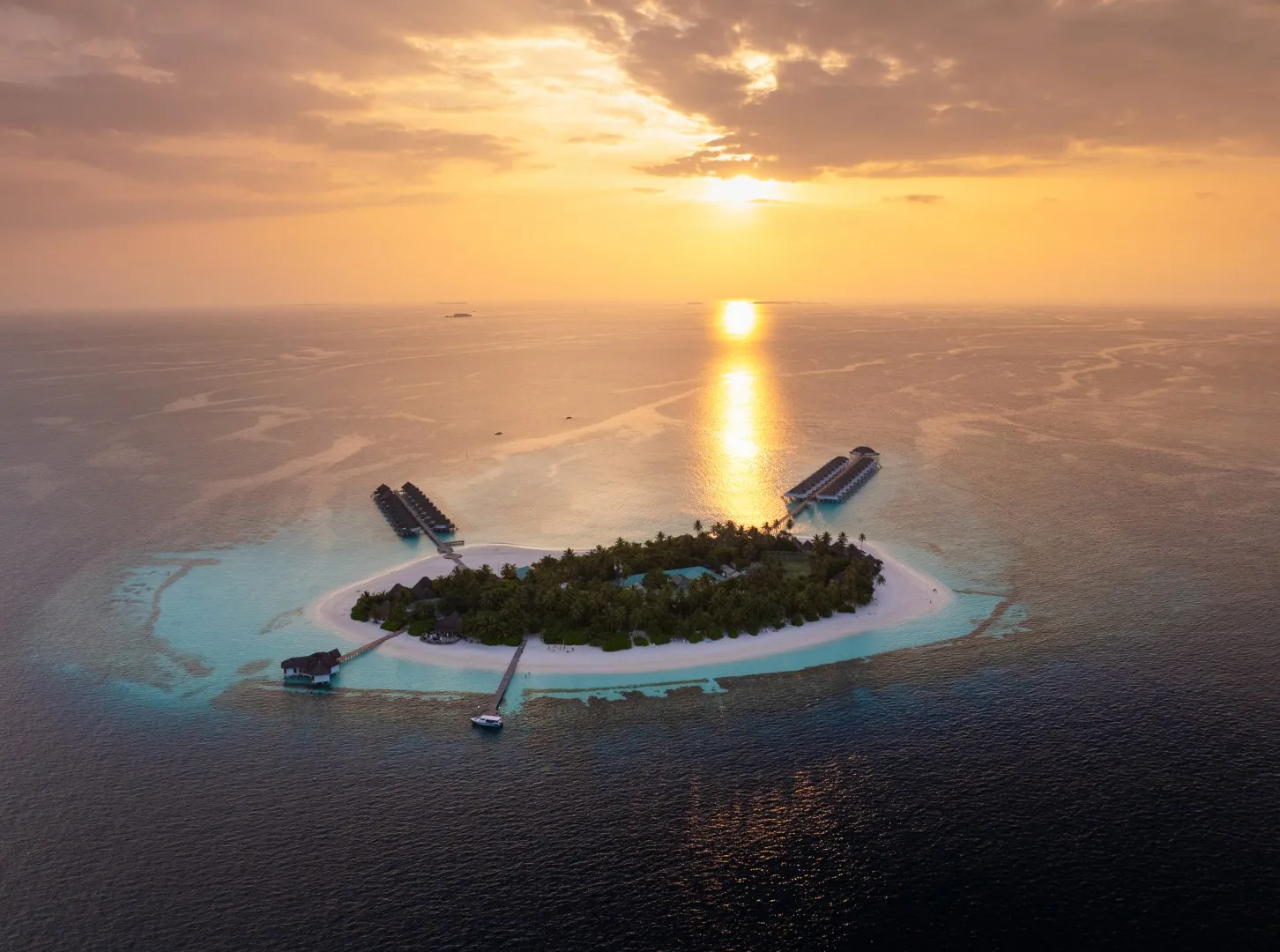 Angaga dall’alto al tramonto: l’isola verde, i 2 pontili dei bungalow sull’acqua e il sole basso sul mare.