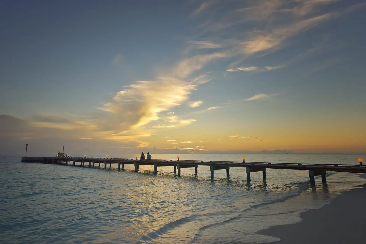Il pontile principale all’alba, con 2 persone sedute in fondo e il cielo che si accende sul mare.