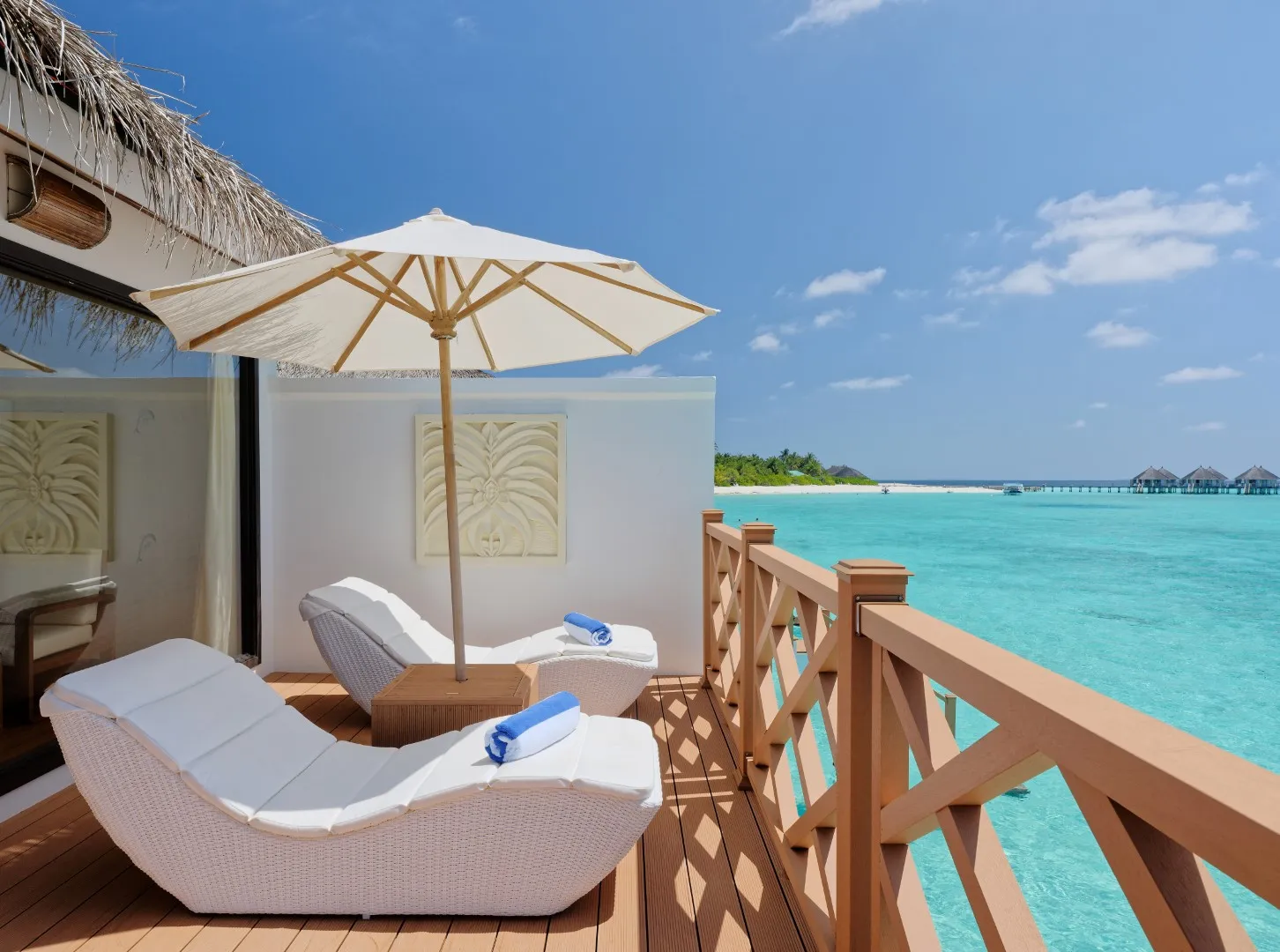La terrazza di un Premium Water Bungalow, con 2 lettini bianchi sotto l’ombrellone e la laguna dietro la balaustra.