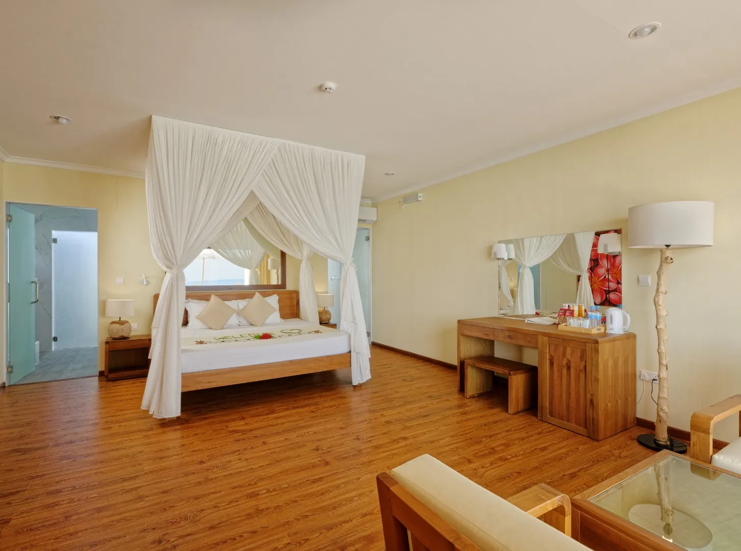 La camera di un Premium Water Bungalow: il letto a baldacchino con il velo bianco, il parquet e il tavolino con il vetro sul mare.